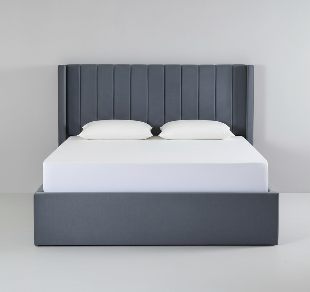 Gray upholstered bed with white mattress and pillows on a plain background