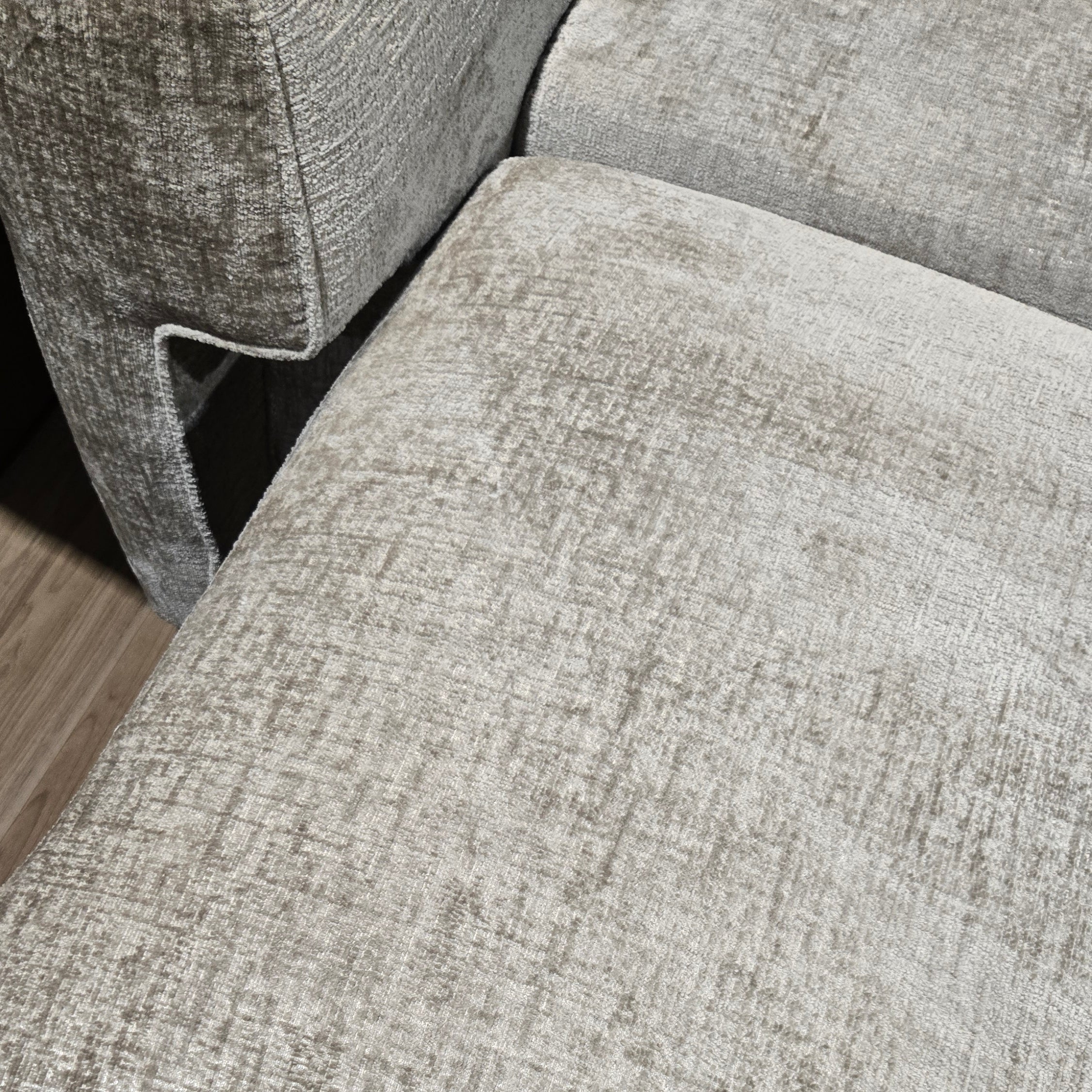 Close-up of a textured gray sofa corner on a wooden floor.